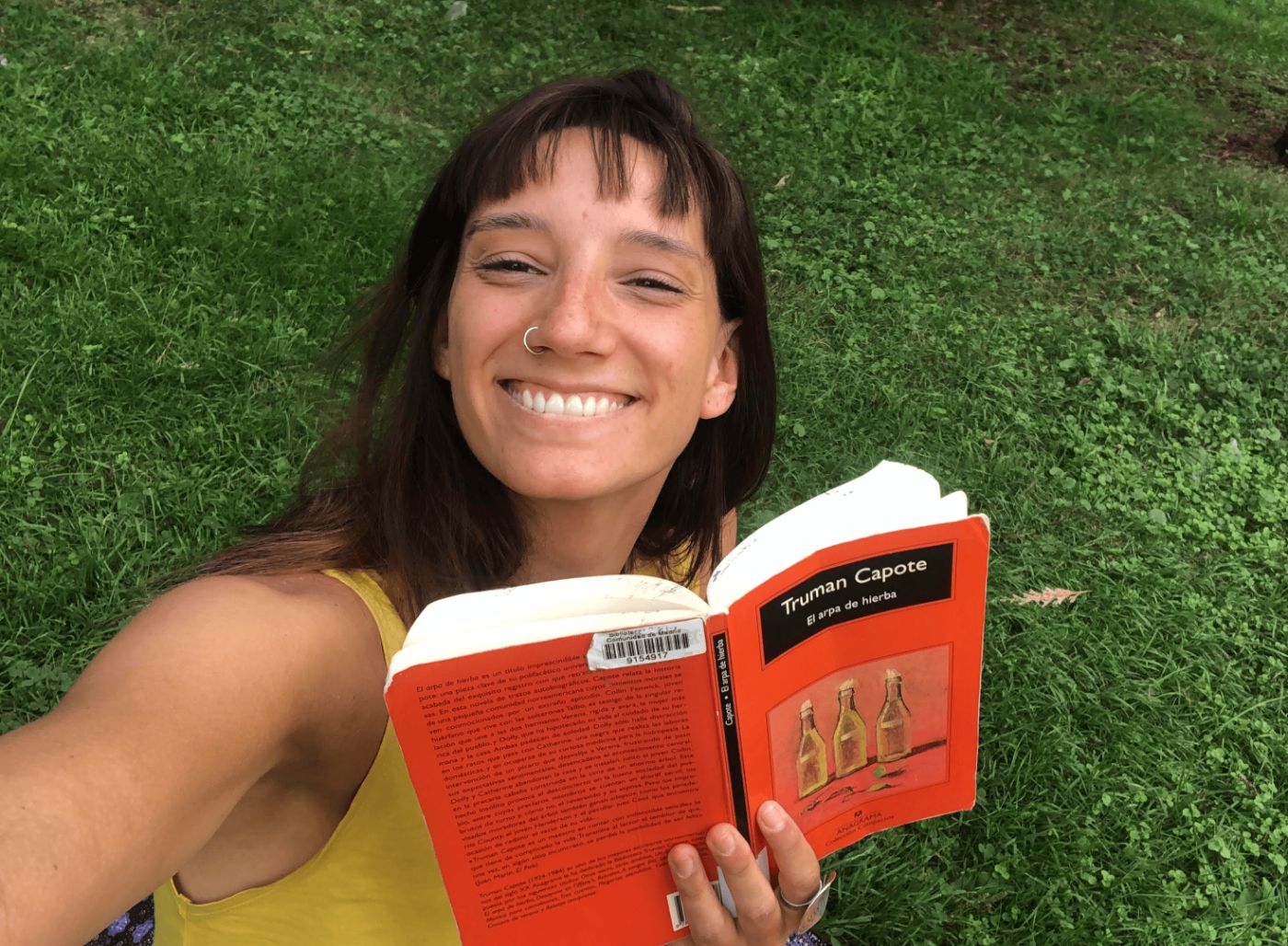 Emilia smiling on the grass, holding a Truman Capote novel